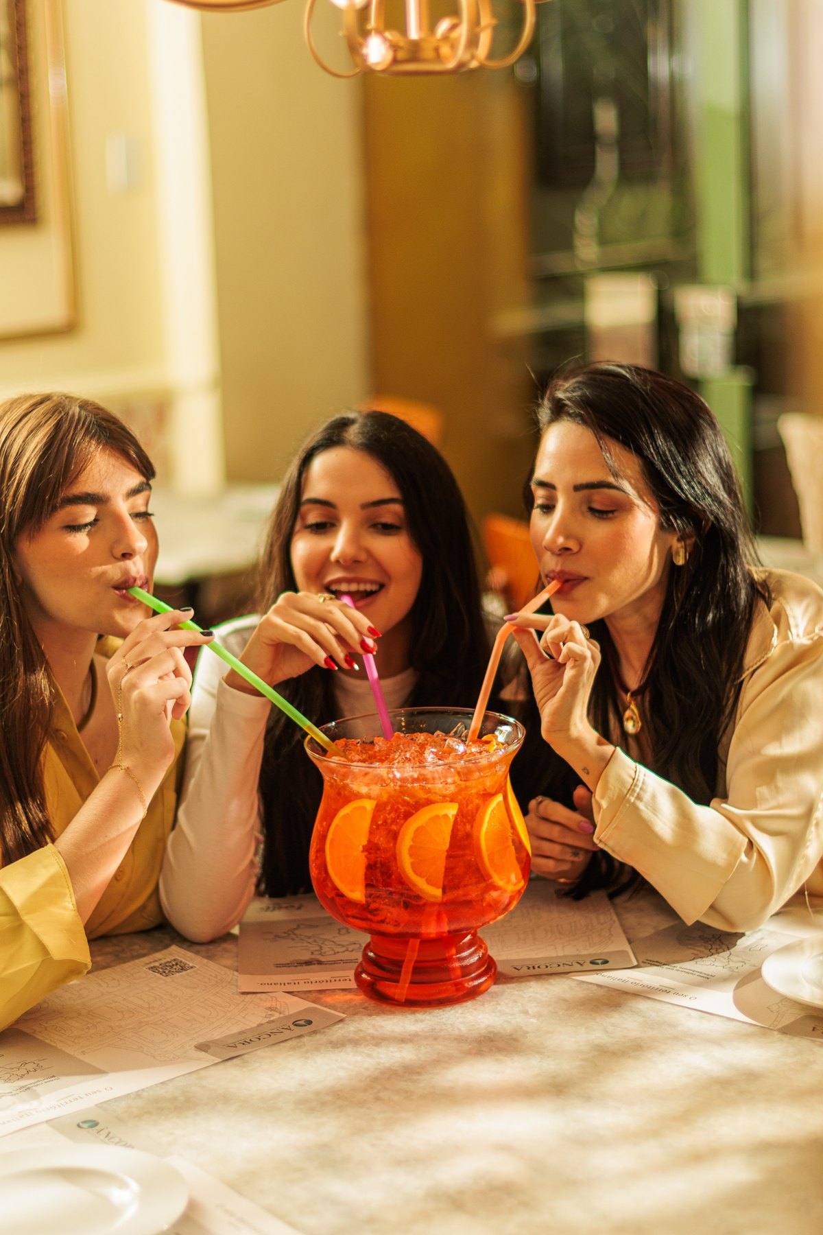 Três amigas dividindo o Aperol Spritz Jumbo com canudos coloridos